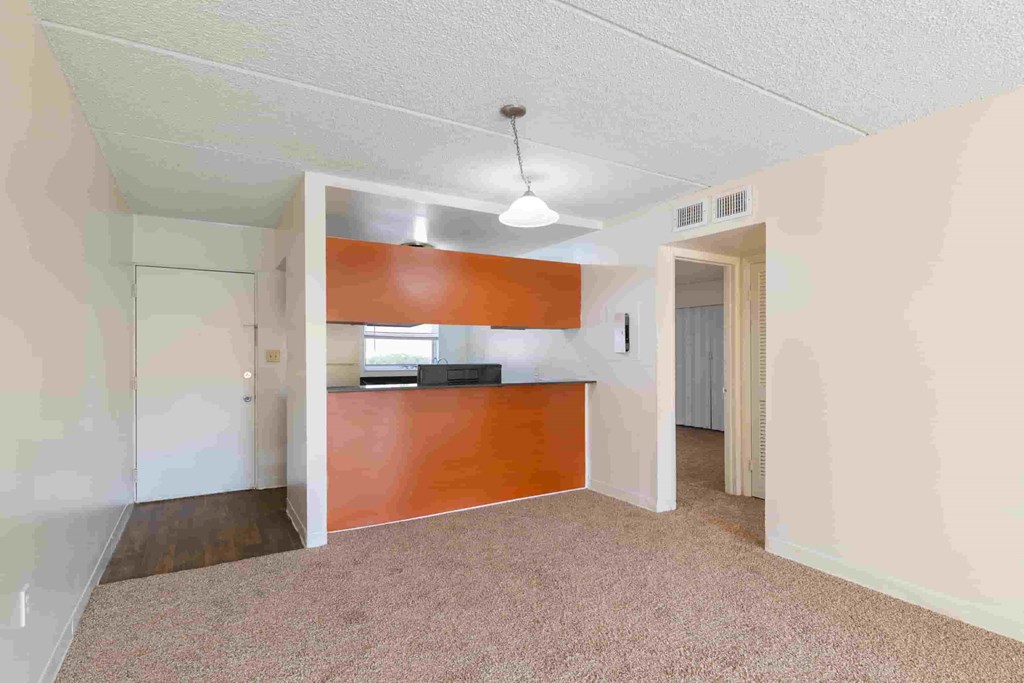 an empty living room with a kitchen in the corner