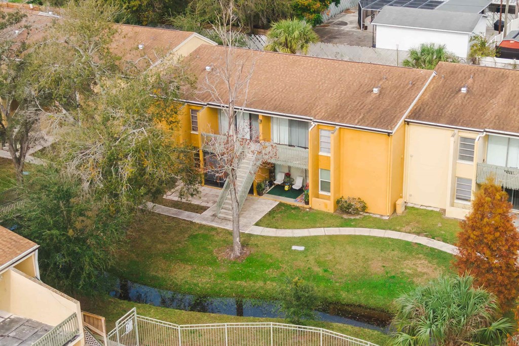 an aerial view of a yellow house with a yard and trees