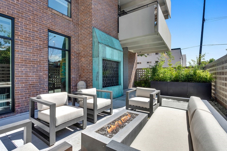 a patio with chairs and a fire pit in front of a brick building