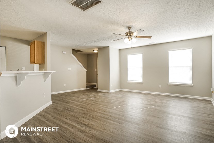 an empty living room with a ceiling fan and a kitchen