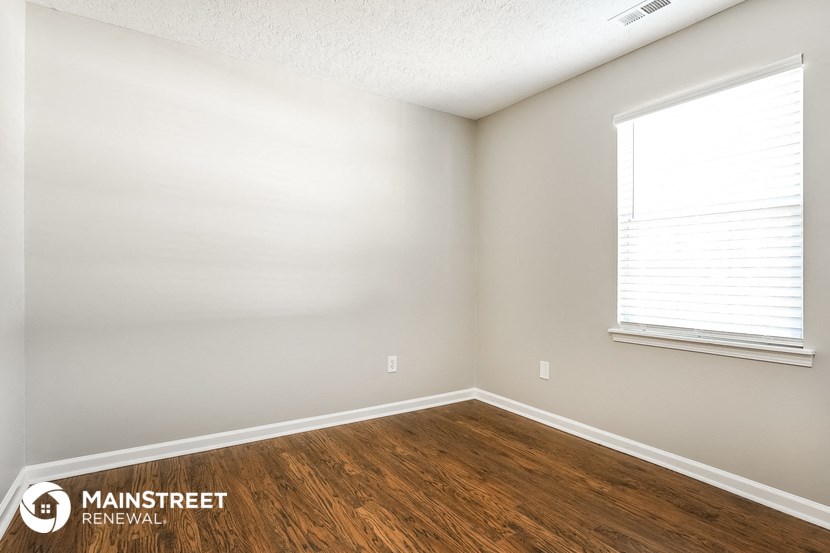 the bedroom of an apartment with wood flooring and a window