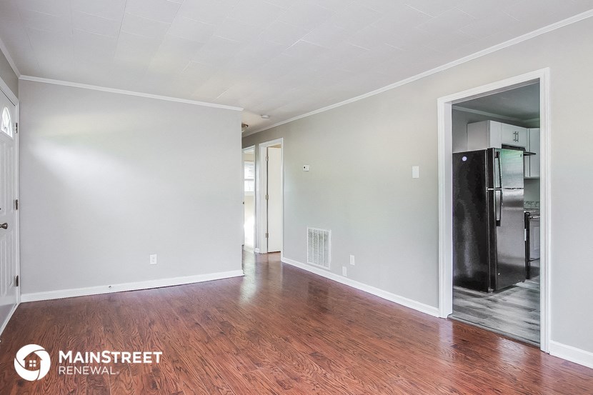 an empty living room with wood flooring and a refrigerator