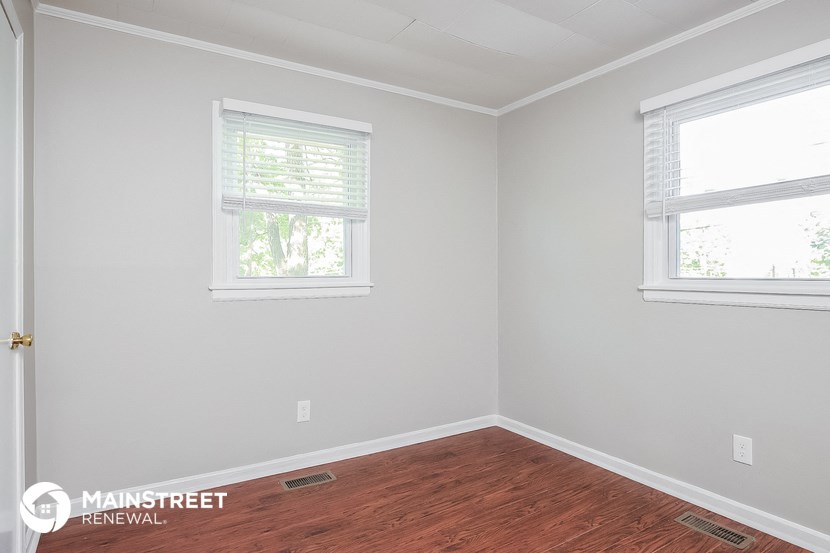 a bedroom with a wooden floor and two windows