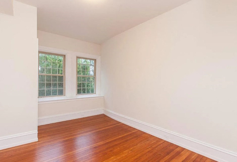an empty room with a hard wood floor and two windows