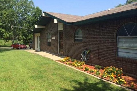 A red car is parked in front of a brick house.