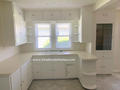 A kitchen with white cabinets and a window with blinds.
