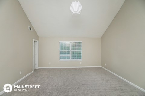 the spacious living room with white carpet and a window