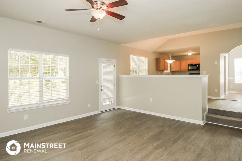 an empty living room with a ceiling fan and a kitchen