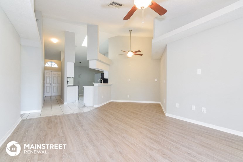 an empty living room with a ceiling fan and a kitchen