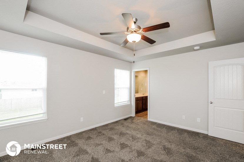 the living room of an apartment with carpet and a ceiling fan
