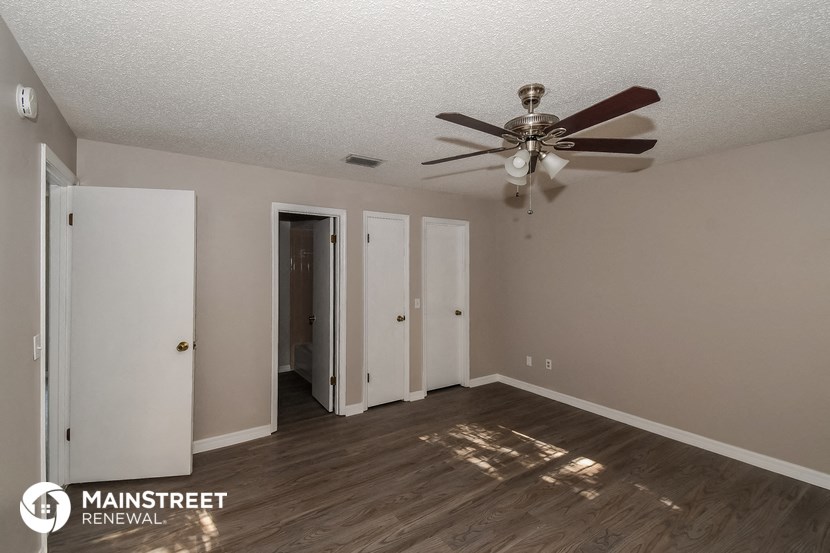 the spacious living room with ceiling fan and door to the hallway