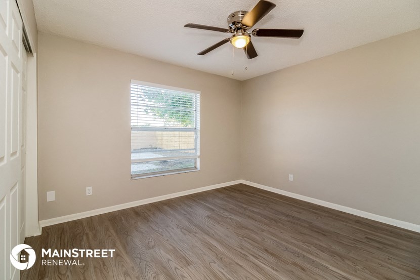 the spacious living room with wood flooring and a ceiling fan