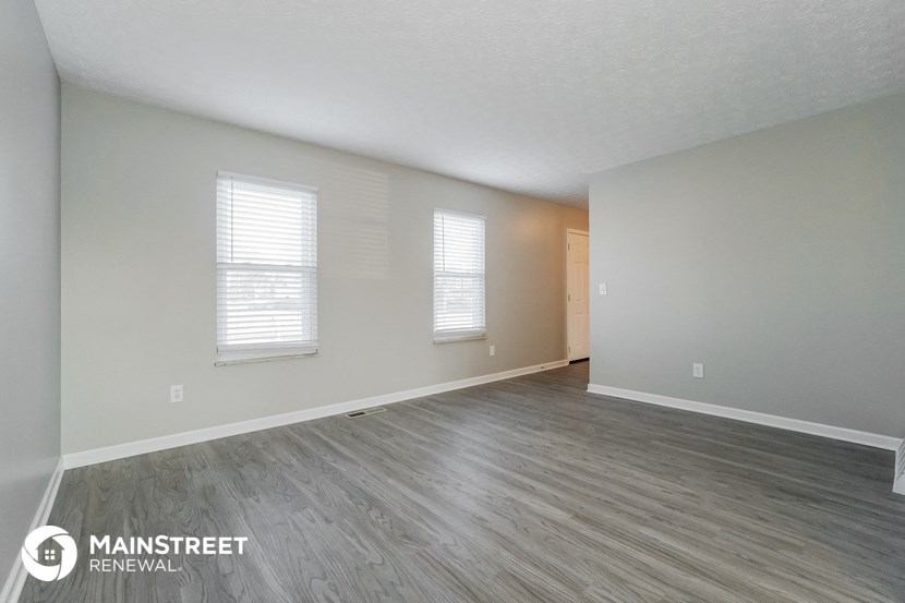 the spacious living room with wood flooring and white walls