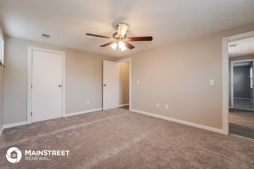 the living room of an apartment with carpet and a ceiling fan