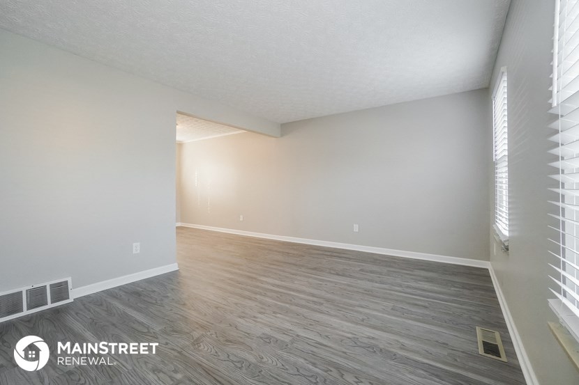 the spacious living room with wood flooring and white walls