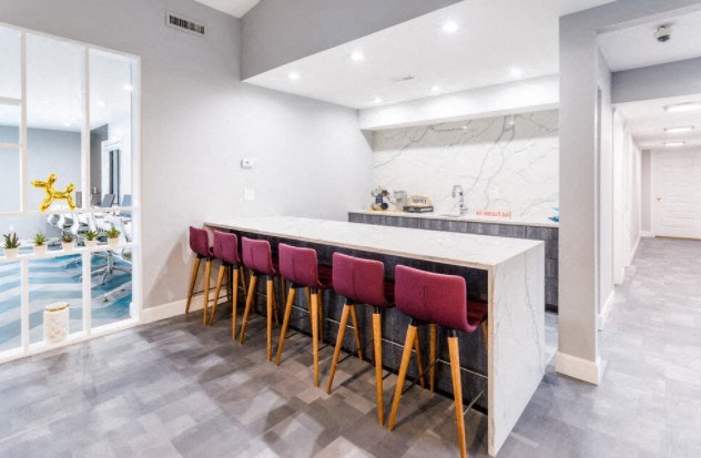 the kitchen has a marble counter top and a row of red chairs