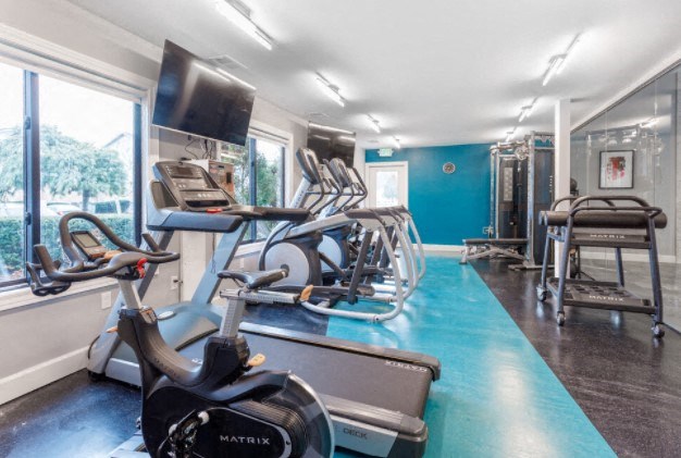 a gym with cardio equipment and a tv on the wall