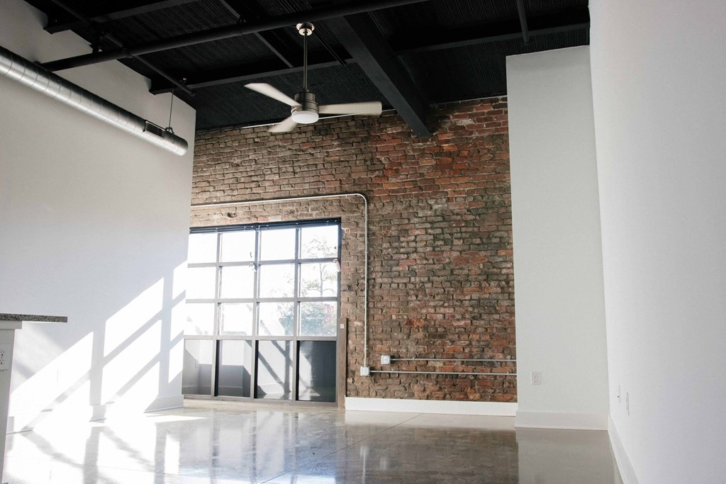 an exposed brick wall in a room with a window and a ceiling fan