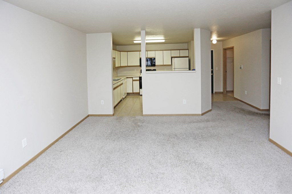 an empty living room and kitchen with white walls and carpet