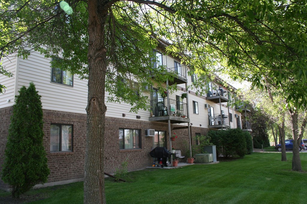 the exterior of an apartment building with a lawn and trees