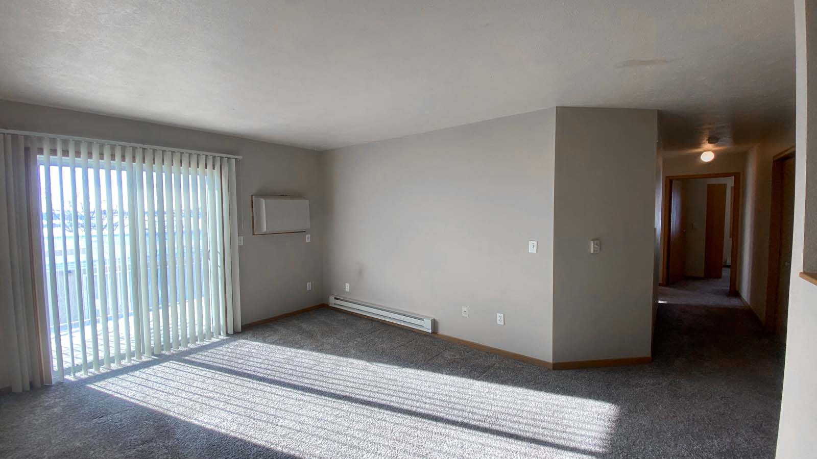 Living room at Amber Fields with heater, in-wall AC unit, patio doors, and view of the hallway