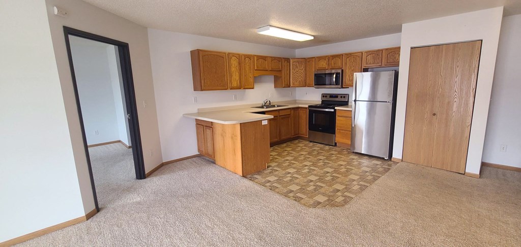 an empty kitchen with wooden cabinets and a stainless steel refrigerator