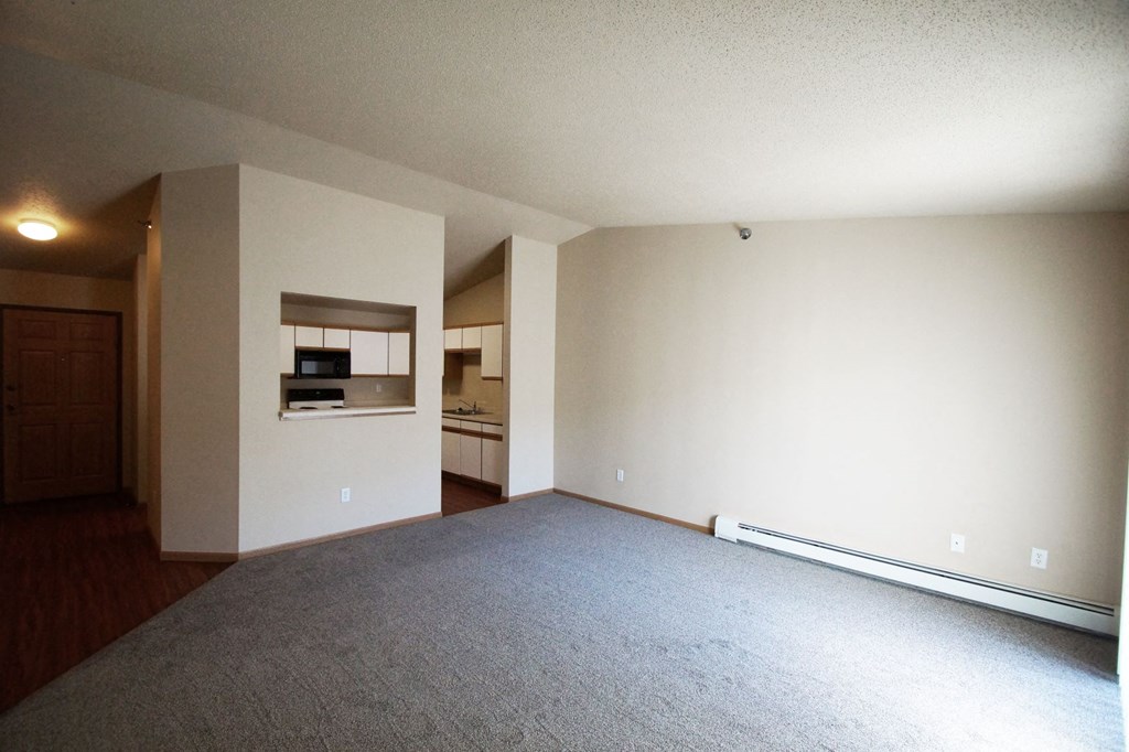 an empty living room with white walls and a kitchen