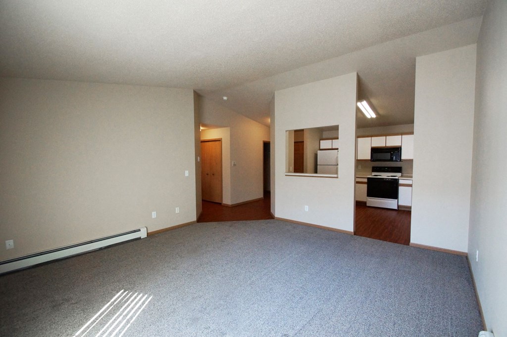 an empty living room with a kitchen in the background