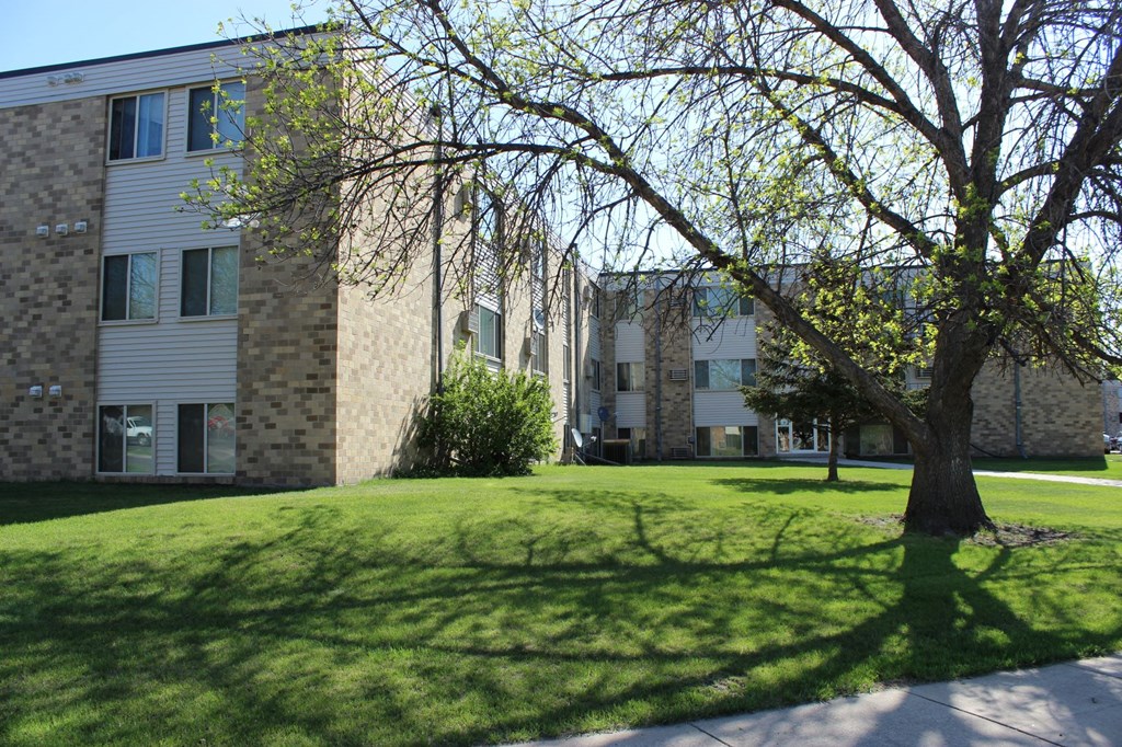an apartment building with a green lawn and a tree