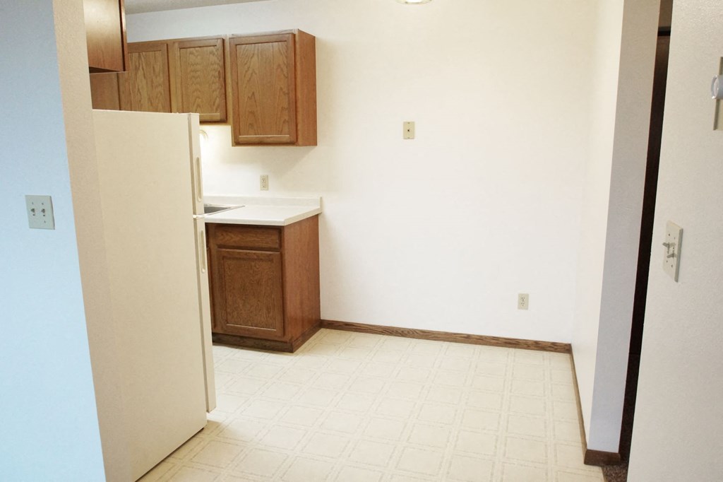 an empty kitchen with wooden cabinets and a refrigerator