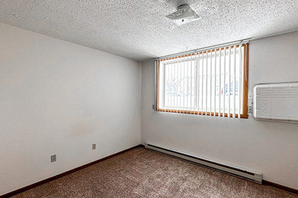 an empty living room with a window and a air conditioner