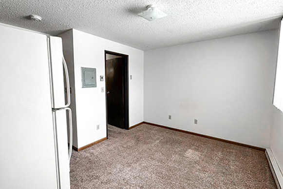 an empty living room with a refrigerator in the corner
