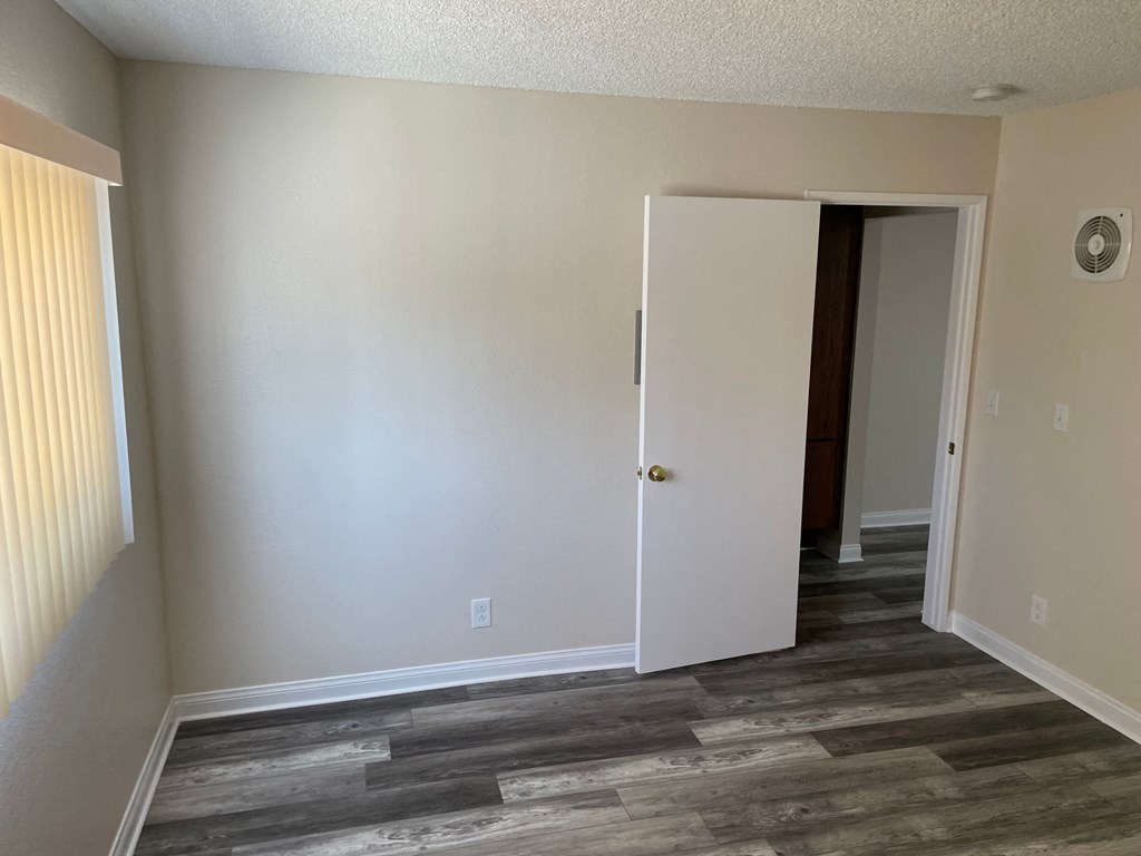 a bedroom with white walls and wood flooring and a closet