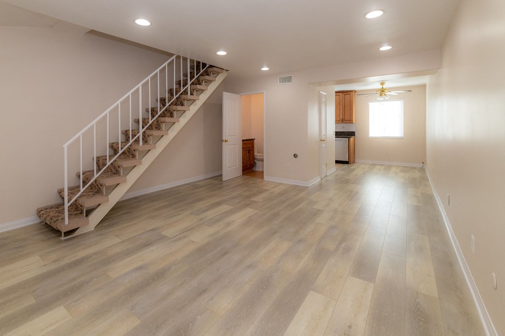 A spacious room with wooden flooring and a staircase.