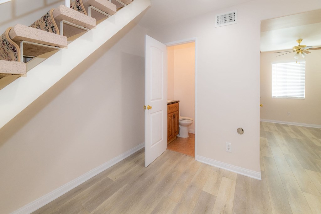 A room with a wooden floor and a white wall with a doorway leading to another room.