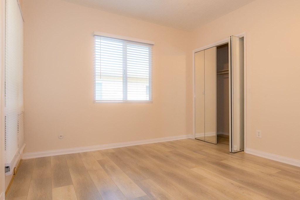 A room with a wooden floor and a window with blinds.
