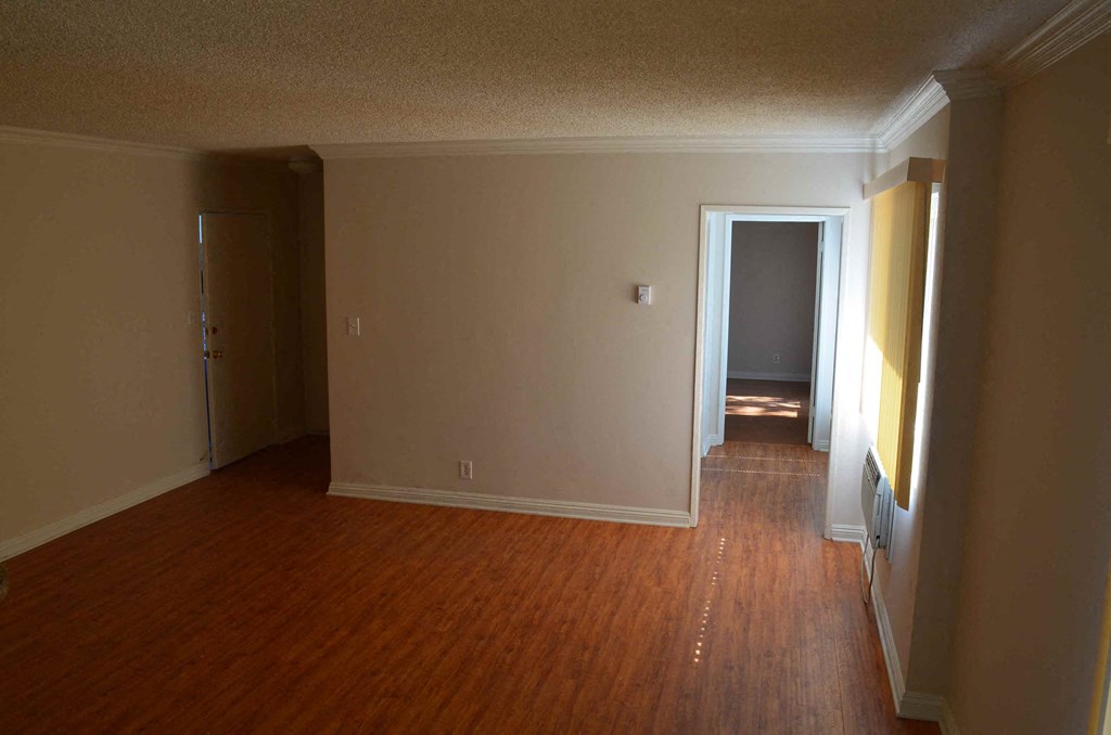 an empty living room with wooden floors and a door to a hallway