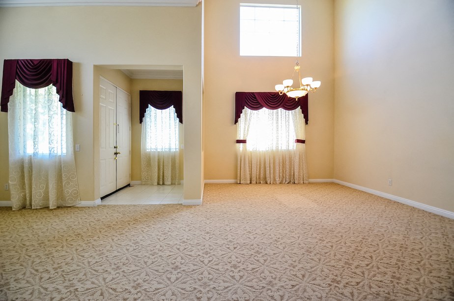 an empty living room with white curtains and a carpet