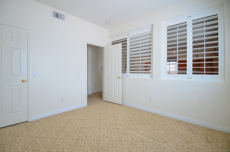 an empty living room with white shuttered windows and a door