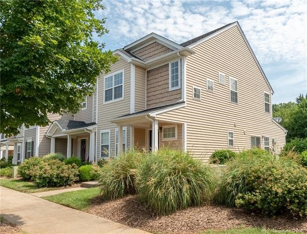 A house with a brown and beige exterior is surrounded by green shrubbery.