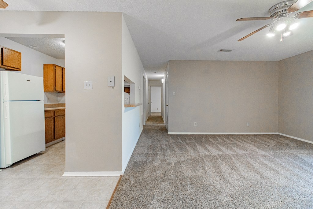 the living room and kitchen of an apartment with a refrigerator and a ceiling fan