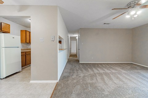 the living room and kitchen of an apartment with a refrigerator and a ceiling fan
