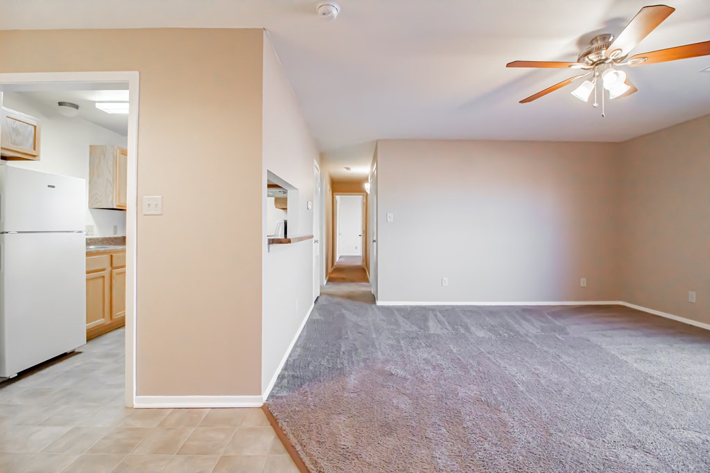 an empty living room with a ceiling fan and a kitchen