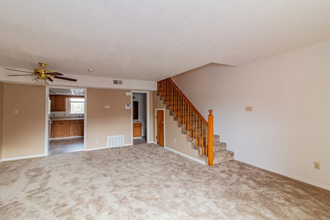 an empty living room with a staircase and a ceiling fan
