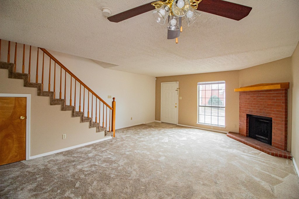 an empty living room with a fireplace and a ceiling fan