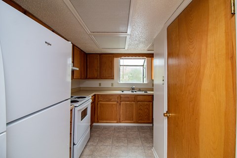 an empty kitchen with white appliances and wooden cabinets
