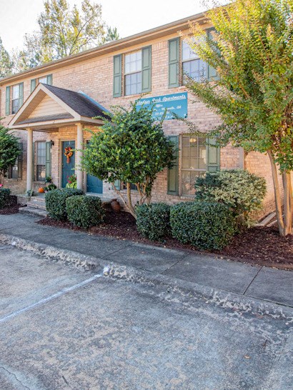 the front of a brick building with a blue sign and trees and bushes