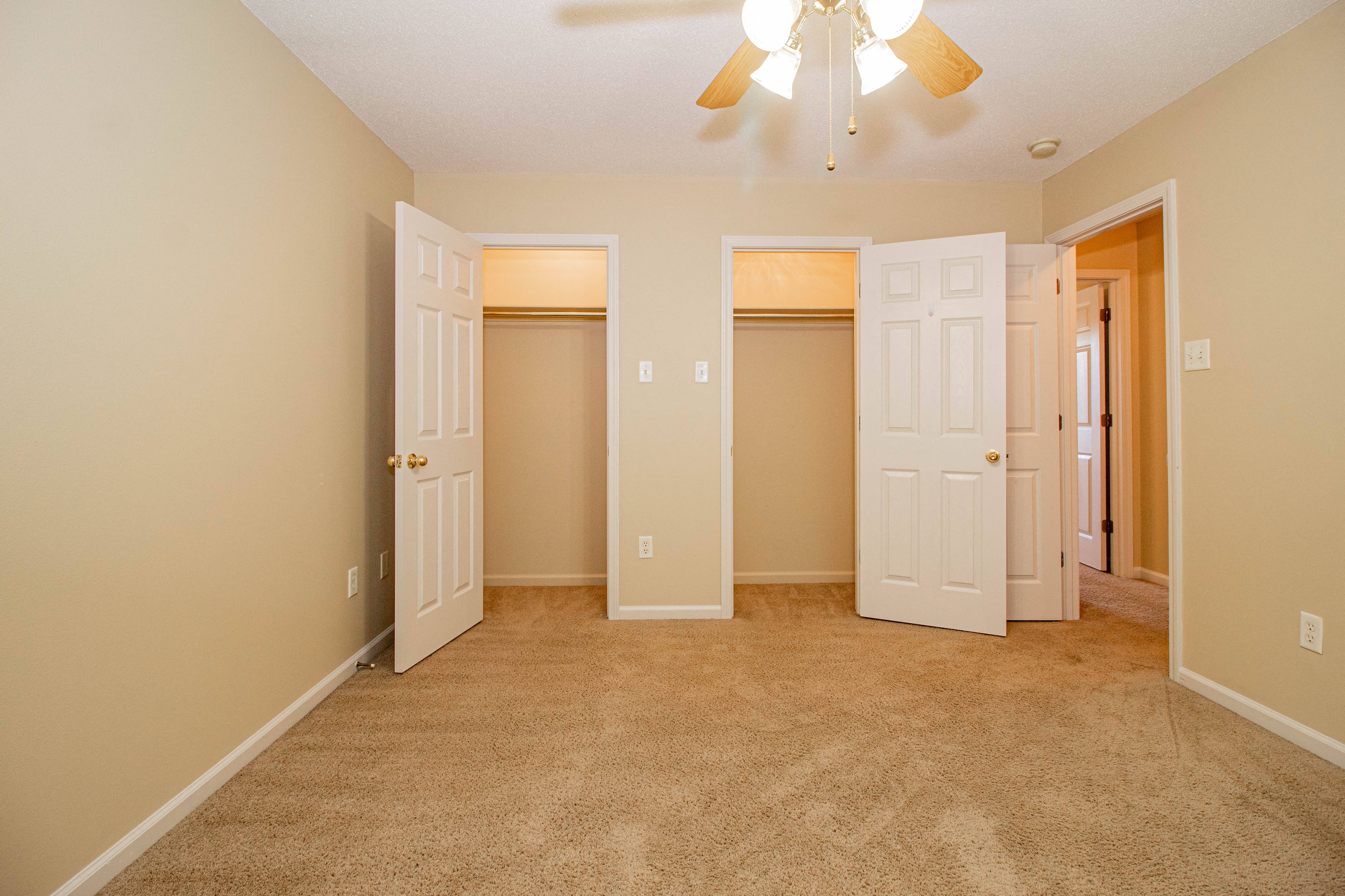 an empty living room with three doors and a ceiling fan