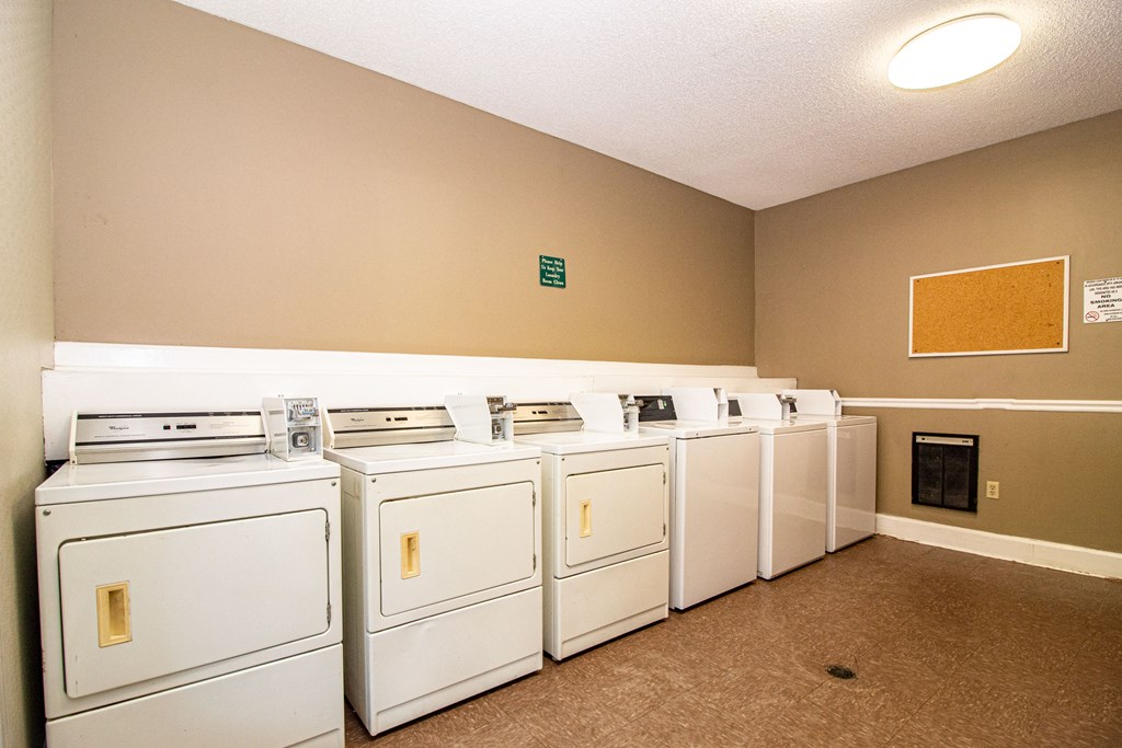 a row of white washers and dryers in a laundry room with a row