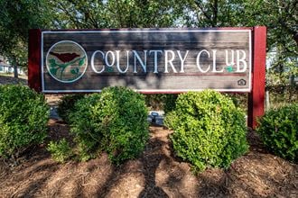 a sign for the country club in front of trees and bushes